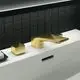 Goldene 3-Loch-Waschtischarmatur von Ideal Standard, bestehend aus einem Wasserhahn und einem Hebel, auf einer weißen Fläche vor schwarzem Fliesenhintergrund.